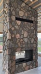 Custom-built natural stone gas fireplace with glass firebox and air vent