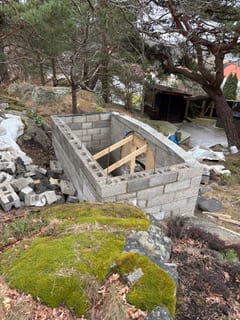 Jordkällarens murade väggar sedda ovanifrån i den kuperade trädgården.